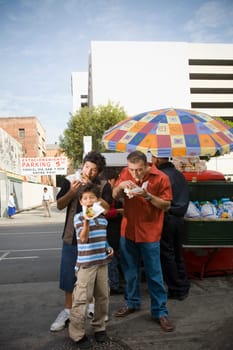 Father and sons eat hot dogs from street vendor