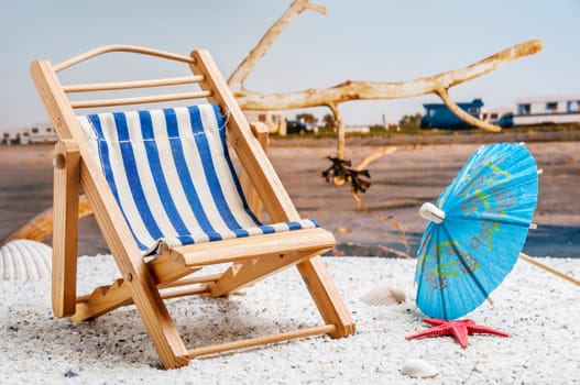 Still life picture composition of a beach scene with a folding deck chair, parasol and red starfish in the foreground and a natural blurred beach scene in the background.