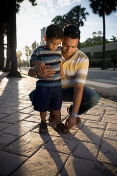 Mid adult man adjusting his son's sandals, Malecon, Santo Domingo, Dominican Republic