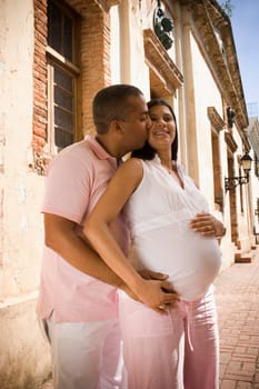 Side profile of a mid adult man embracing and kissing a pregnant young woman from behind, Santo Domingo, Dominican Republic
