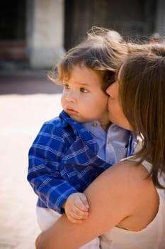 Side profile of a mid adult woman carrying and kissing her son
