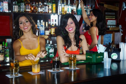 Three sexy young waitresses serve drinks behind bar