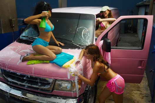 Three sexy young women washing a pink van in car wash