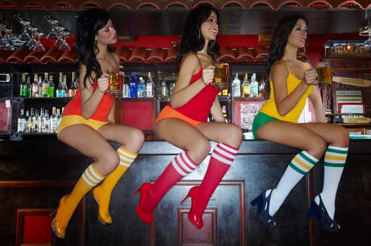 Three sexy young waitresses sitting on bar counter