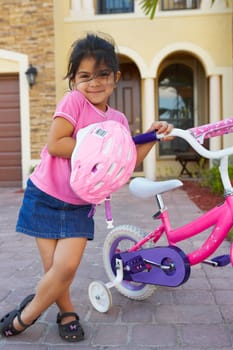 Portrait of a girl standing and holding a bicycle in front of a house