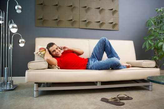Young man talking on a mobile phone and lying on a couch