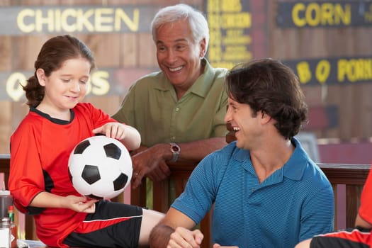 Close-up of a girl holding a soccer ball with her father and grandfather looking at her
