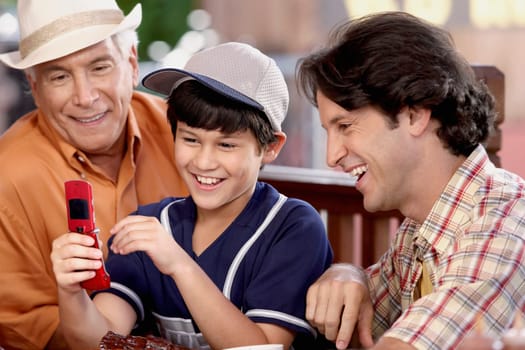 Close-up of a senior man with his son and grandson looking at a mobile phone and smiling