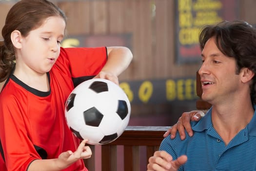 Close-up of a girl playing with a soccer ball with her father looking at her