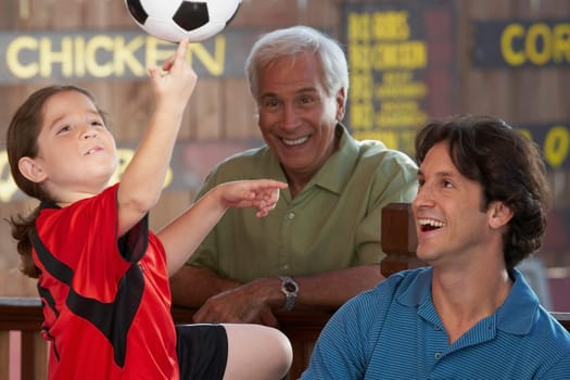 Close-up of a girl playing with a soccer ball with her father and grandfather beside her
