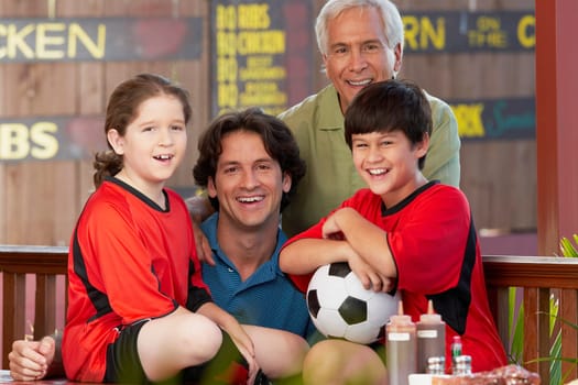 Portrait of a boy and a girl with their father and grandfather sitting in a restaurant and smiling