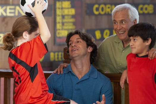 Side profile of a girl holding up a soccer ball with her family looking at her in a restaurant