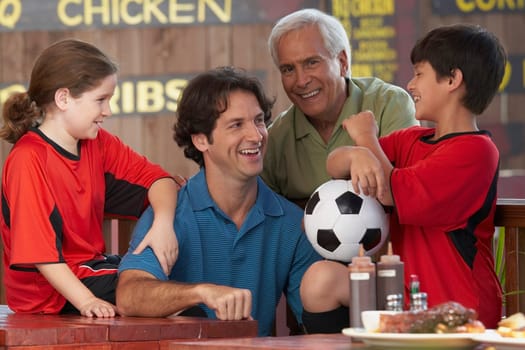 Boy and a girl with their father and grandfather sitting in a restaurant and smiling
