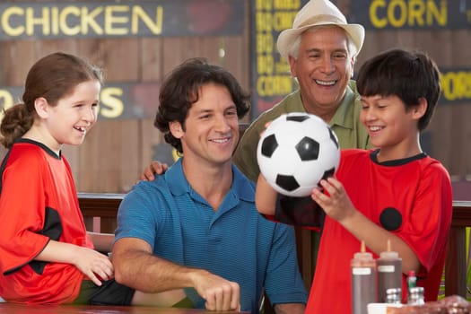 Boy playing with a soccer ball with his family beside him in a restaurant