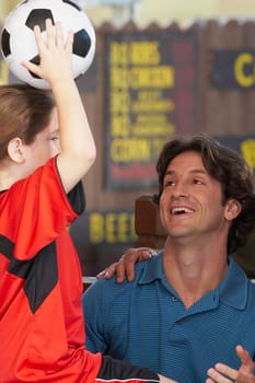 Close-up of a girl holding up a soccer ball with her father looking at her