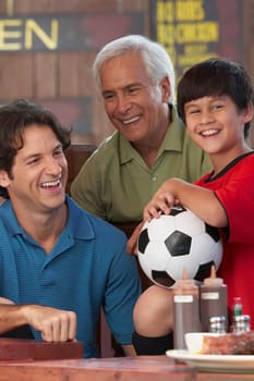 Senior man with his son and grandson sitting in a restaurant and smiling