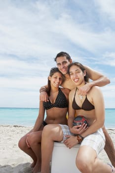 Portrait of two young women sitting on an ice box with a young man standing behind them