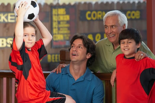 Portrait of a girl holding up a soccer ball with her family beside her in a restaurant