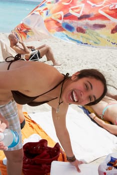 Portrait of a young woman holding a bottle on the beach and laughing