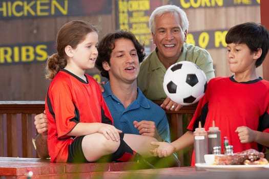 Boy playing with a soccer ball with his family beside him in a restaurant