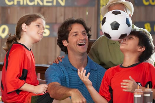 Boy playing with a soccer ball with his family looking at him in a restaurant