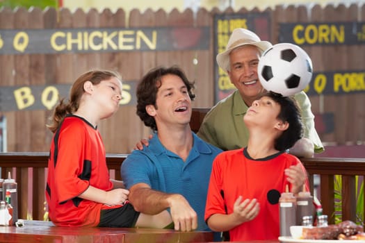 boy balancing a soccer all on his head with his family looking at him