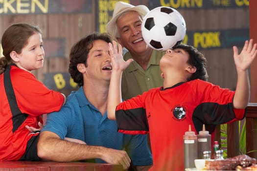 boy balancing a soccer all on his forehead with his family looking at him