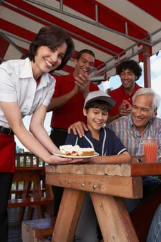 Portrait of a young woman serving dessert to a boy celebrating his birthday in a restaurant