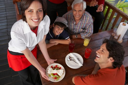 Portrait of a young woman serving dessert to a mid adult man celebrating his son's birthday in a restaurant