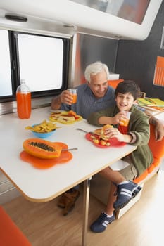 Senior man with his grandson drinking juice and smiling at the dining table