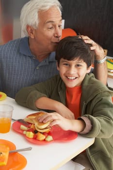 Portrait of a boy holding a burger with his grandfather kissing him on his head