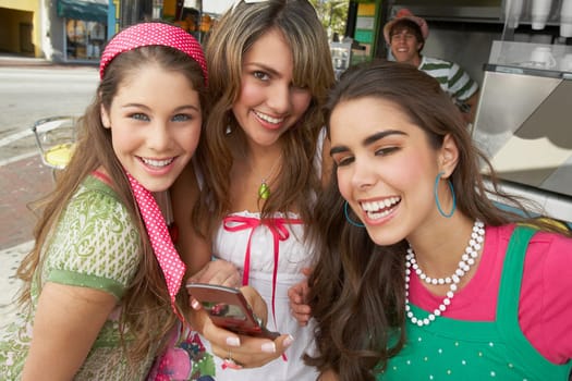 Close-up of a teenage girl holding a mobile phone and standing with her friends