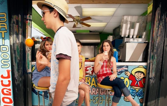 Teenage girl drinking juice with her two friends and a teenage boy tossing a orange in front of them