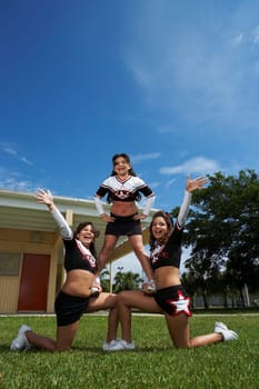 Low angle view of three cheerleaders balancing in a lawn
