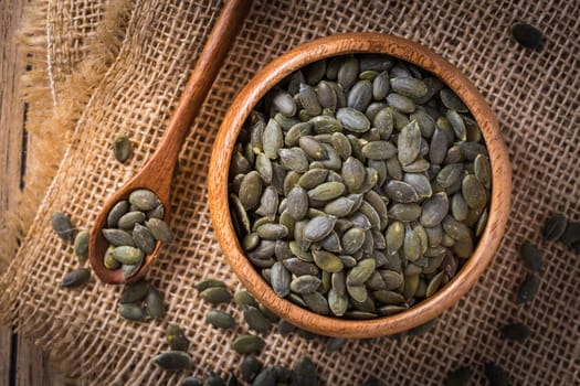 Organic pumpkin seeds in bowl on wooden background