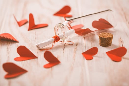 Love message in a bottle with paper hearts on wooden background -happy Valentine