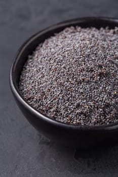 Poppy seeds in black bowl on dark background