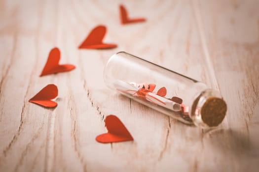 Love message in a bottle with paper hearts on wooden background -happy Valentine