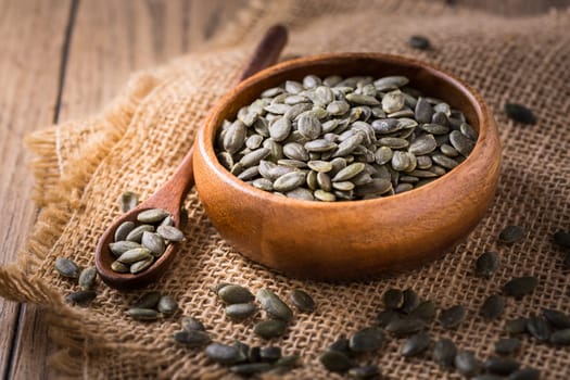 Organic pumpkin seeds in bowl on wooden background