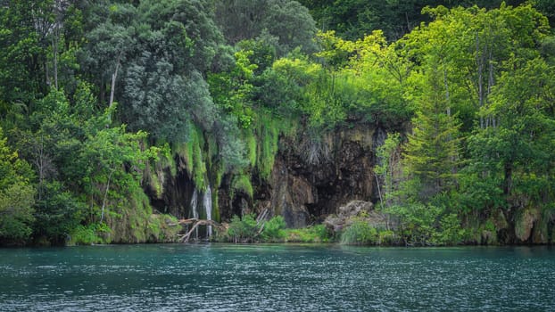 Closeup on waterfall and cave on the edge of turquoise lake. Green lush forest in Plitvice Lakes National Park UNESCO World Heritage, Croatia