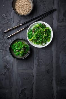 Traditional Japanese wakame salad with sesame seeds on black background. Healthy and fresh seaweed salad.