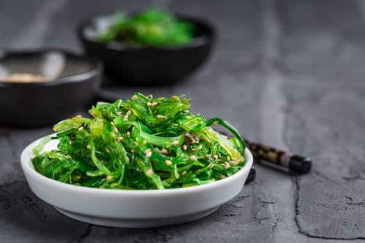 Traditional Japanese wakame salad with sesame seeds on black background. Healthy and fresh seaweed salad.
