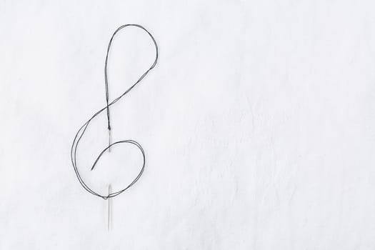 Macro of sewing needle in white fabric in violin key shape. Concept of handcraft and art. Copy space for your text.