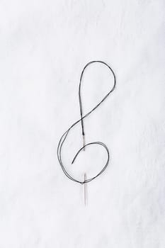 Macro of sewing needle in white fabric in violin key shape. Concept of handcraft and art.