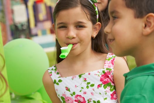 Close-up of a girl with a party horn blower in her mouth and her two friends beside her