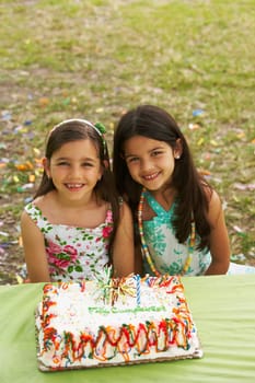 Two girls sitting in front of a birthday cake