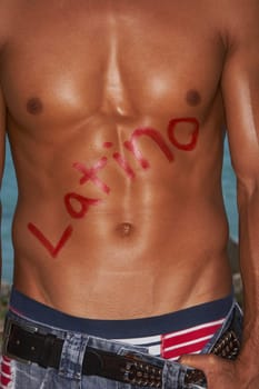 Mid section view of a bare chested young man with Latino written on his chest