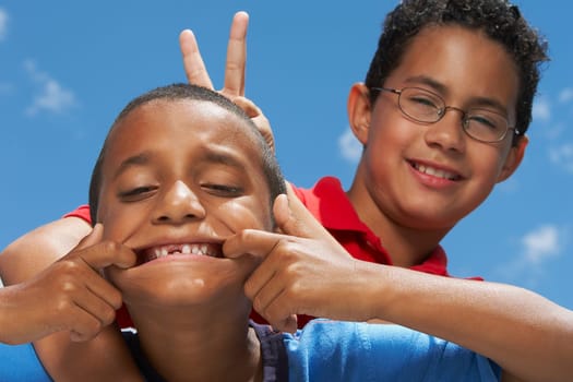 Close-up of a boy making a face with his friend making a gesture of rabbit ears from behind