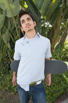 Young man holding a skateboard behind his back