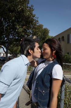 Side profile of a young man kissing a young woman leaning against a chain-link fence